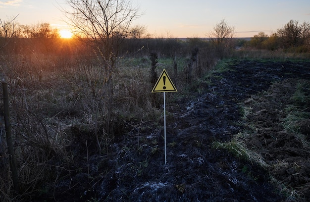 Verbranntes trockenes Gras und Warnschild mit Ausrufezeichen warnt vor Gefahr auf dem Feld bei Sonnenuntergang Konzept der Ökologie und Naturkatastrophe