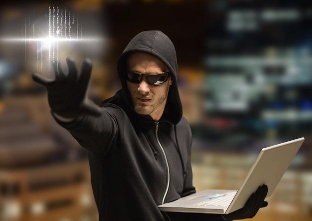 Verbrecher in Kapuze auf Laptop vor Nachtstadt