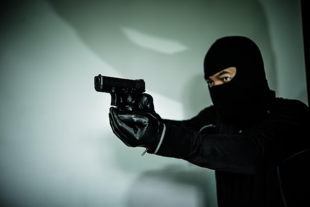 Verbrecher mit Waffe in der Hand auf weißem HintergrundLow-Key-Stildunkler Tonselektiver Fokus