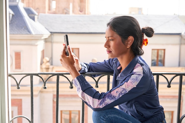 Verbunden und unterhalten Junge indische Frau genießt ihr Telefon, während sie auf der Fensterbank sitzt