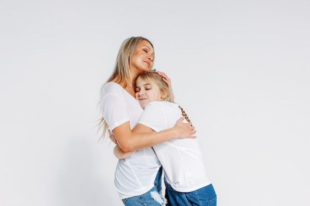 Verdadeira mãe e filha em camisetas brancas e jeans abraçando isolado no fundo branco