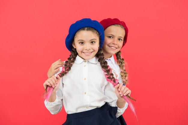 Los verdaderos amigos siempre están a tu lado. La amistad significa apoyo. Mejores amigas de chicas sobre fondo rojo. Colegialas lindas hermanas juguetonas que se divierten. Niños trenzas largas peinado amigos compañeros de clase.