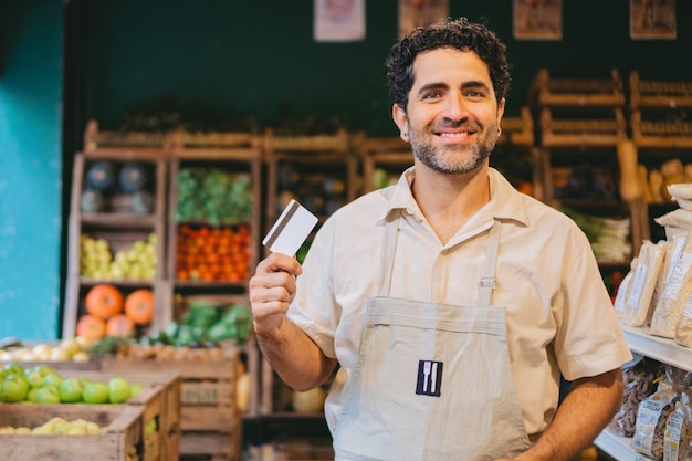 Verdulero latino de mediana edad mirando a la cámara mientras sostiene la tarjeta de crédito en la mano Copiar espacio