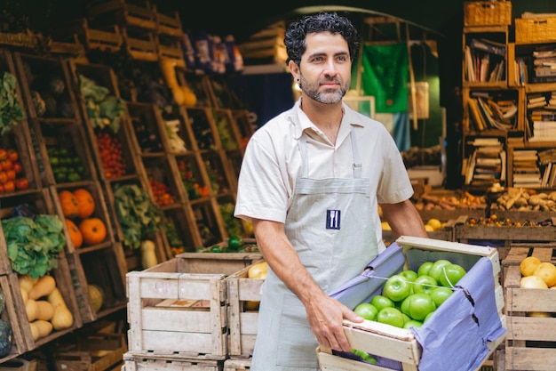 Verdulero latino de mediana edad en su tienda orgánica con manzanas verdes en las manos