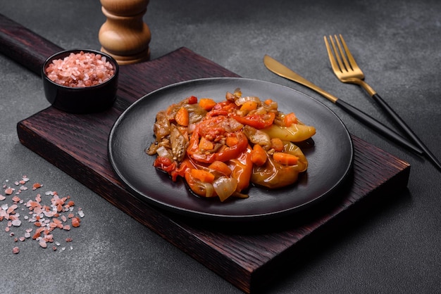 Verduras al horno berenjena pimientos y zanahorias en un plato negro sobre fondo de hormigón