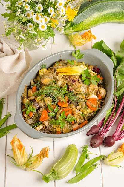 Verduras al horno con hierbas en un plato para hornear sobre un fondo blanco de madera