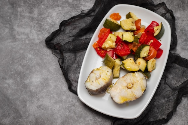 Verduras al horno con pescado hervido en plato blanco