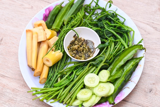 Verduras al vapor en un plato y fondo de madera Comida asiática tailandesa con verduras al vapor o hervidas con pepino Brotes de bambú Acacia pennata Okra Frijol alado Ceilán Espinacas y salsa de chile