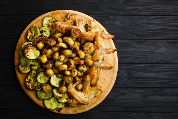 Verduras y alitas de pollo asadas a la parrilla en la placa de madera. Espacio libre.