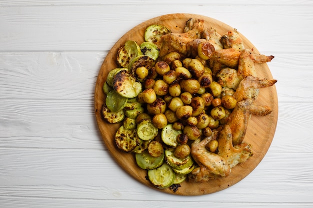 Verduras y alitas de pollo asadas a la parrilla en la placa de madera. Espacio libre.