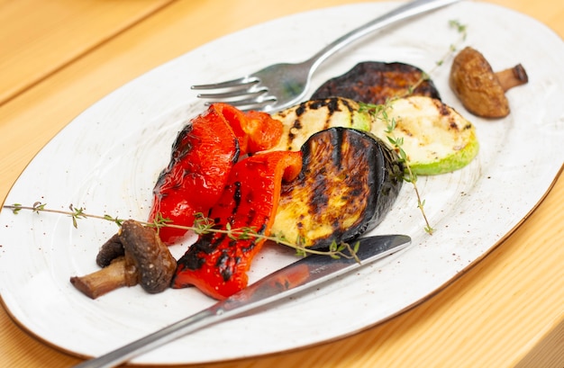 Verduras asadas en un plato blanco, un tenedor y un cuchillo sobre la mesa en un restaurante