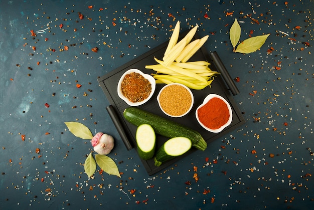 LAS VERDURAS EN LA CAJA EN LA PIEDRA UN OSCURO. JÓVENES VERDES CEBOLLA AJO ZUCCHINI ESPECIAS BRILLANTES COLOCA EN UNA BANDEJA DE MADERA CON MANGOS EN UN OSCURO TEXTURADO.