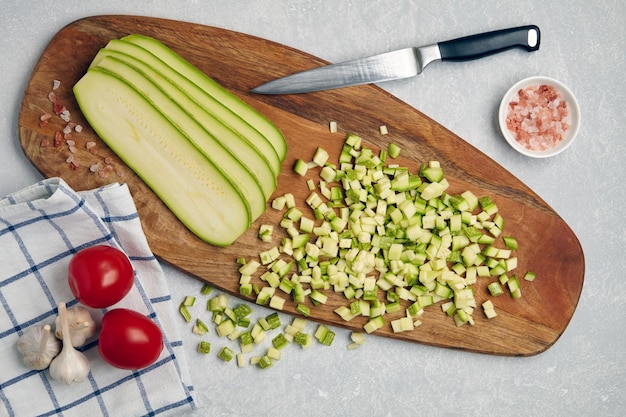 Verduras de calabacín calabacín en rodajas sobre una tabla de cortar de madera tomates ajo rosa sal y servilleta sobre una mesa de luz de hormigón Vista superior plana