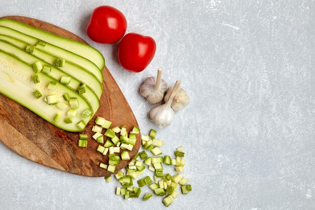 Verduras de calabacín en rodajas sobre una tabla de cortar de madera tomates y ajo sobre una mesa de luz de hormigón Vista superior con espacio de copia Lay Flat