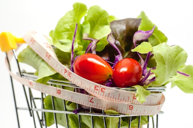 Verduras en el carrito de compras con cinta métrica sobre fondo blanco