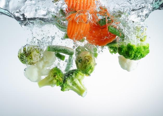 Foto verduras cayendo al agua con salpicaduras y burbujas de aire. cocinar comida vegetariana.