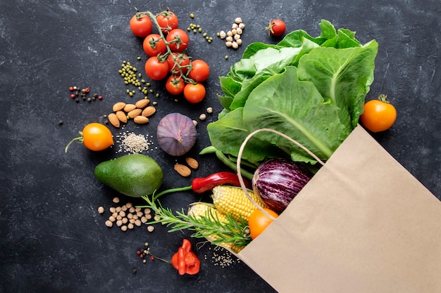 Verduras y cereales en una bolsa de papel sobre una superficie negra. El concepto de una canasta de consumo, compras en línea, alimentos saludables.