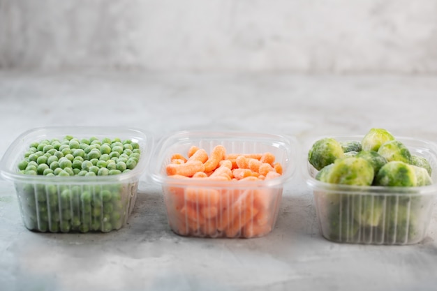 Foto verduras congeladas como guisantes verdes, coles de bruselas y zanahoria pequeña en las cajas de almacenamiento en el espacio gris concreto