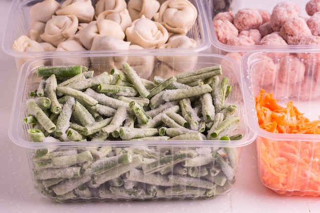 Verduras congeladas y productos cárnicos semiacabados en recipientes de plástico sobre un plato blanco. albóndigas, albóndigas, frijoles picados y zanahorias ralladas