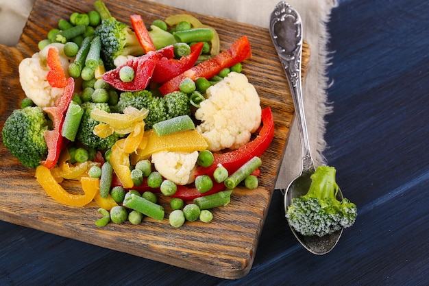 Verduras congeladas en tabla de cortar en servilleta sobre fondo de mesa de madera