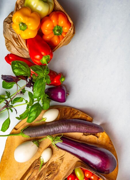 Verduras crudas en bolsas de papel ecológico en la mesa blanca vista de tomates frescos albahaca berenjena pimientos Concepto de alimentación saludable