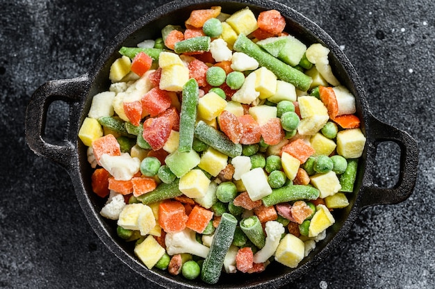 Verduras crudas congeladas en una sartén. Vegetarianismo. Fondo negro. Vista superior.