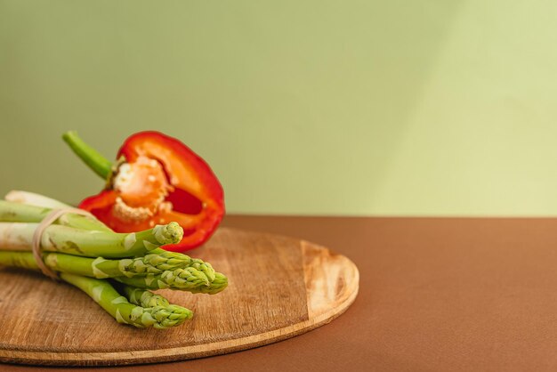 Las verduras se encuentran en una tabla de madera, espárragos, pimientos rojos, marrón, fondo verde claro, lugar para el texto