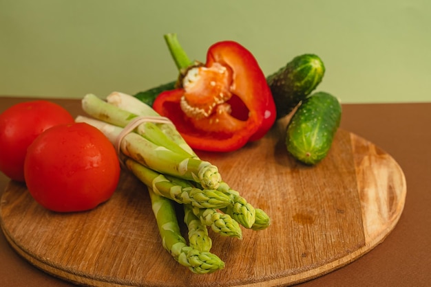 Las verduras se encuentran en una tabla de madera, tomates, espárragos, pepinos, pimientos rojos, marrón, fondo verde claro, lugar para texto