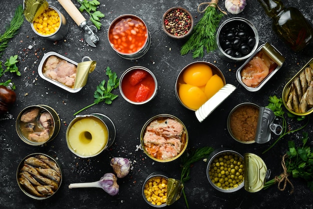 Verduras enlatadas frijoles pescado y frutas en latas sobre fondo de piedra negra Existencias de alimentos