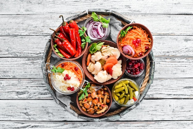 Verduras en escabeche y champiñones en una mesa de cocina blanca Col champiñones pepinos coliflor Vista superior Espacio libre para el texto