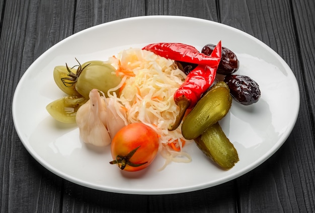 Verduras en escabeche surtidas en un plato. En una mesa oscura