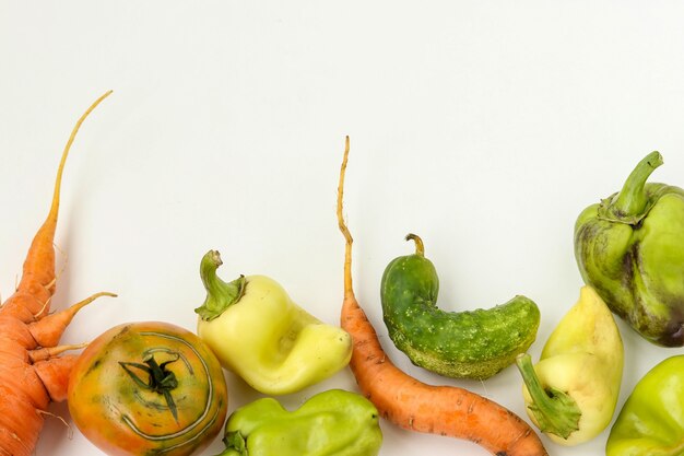 Verduras feas: zanahorias, pepinos, pimientos y tomates sobre fondo blanco, concepto de comida fea, foto horizontal, espacio de copia