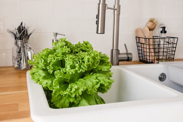 Verduras frescas y albahaca en el fregadero de la cocina blanca