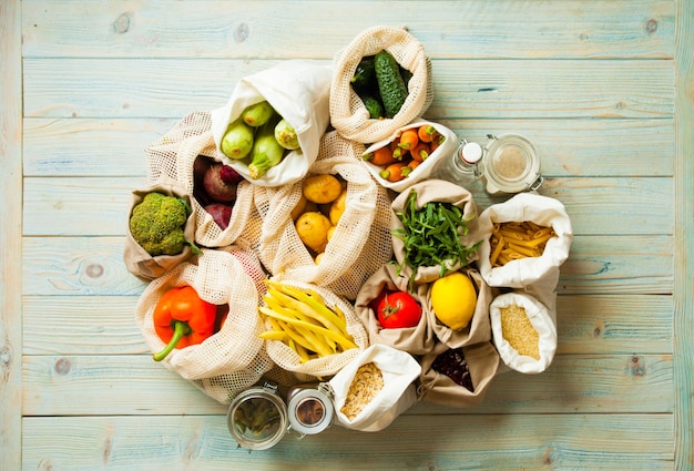 Verduras frescas en bolsas de malla de algodón sobre la mesa de madera azul. Compra de alimentos en el mercado, consumo consciente, prohibición de plástico.