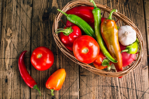 Verduras frescas en una cesta sobre un fondo de madera, pimiento, ajo, tomates