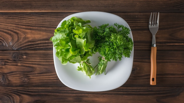 Verduras frescas em um prato branco e um garfo em uma mesa de madeira. O conceito de alimentação saudável. Postura plana.