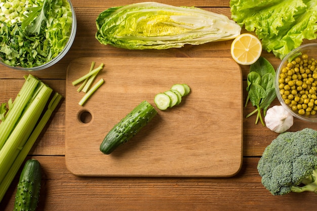 Verduras frescas para ensalada en una mesa de madera con una tabla para cortar. Vista superior.