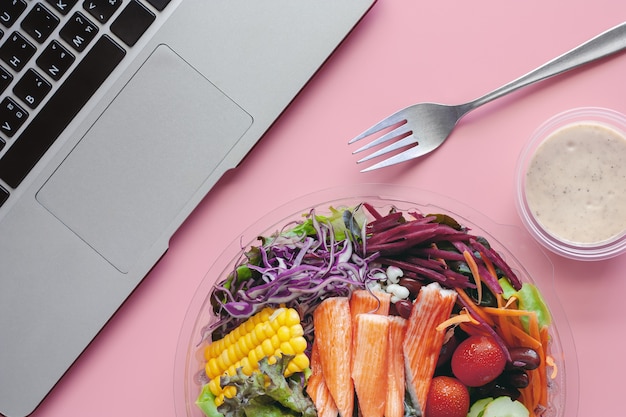 Foto verduras frescas de la ensalada con el ordenador portátil en el lugar de trabajo