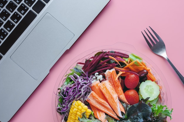 Verduras frescas de la ensalada con el ordenador portátil en el lugar de trabajo