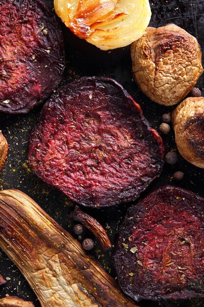 Verduras frescas guisadas horneadas en el horno Rodajas de cebolla de berenjena de remolacha al horno con granos de pimienta de especias sobre un fondo oscuro Primer plano