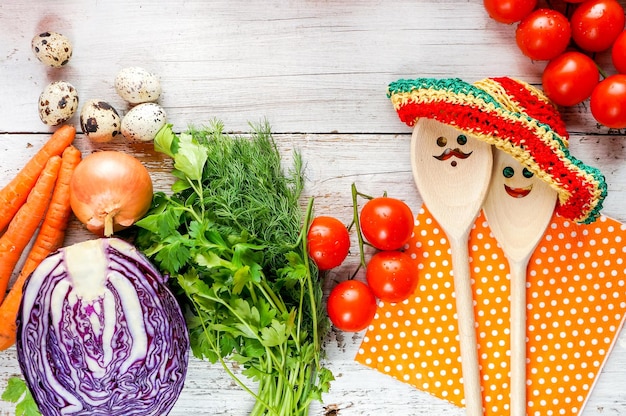 Verduras frescas en una mesa de madera con cucharas divertidas con caras y sombreros de verano