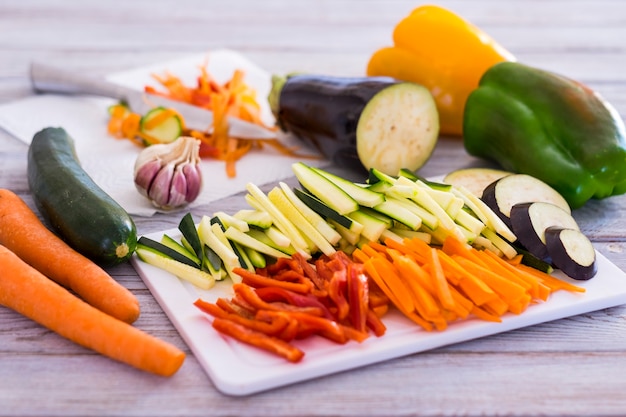 Verduras frescas en una mesa de madera con una mezcla de zanahorias en rodajas, calabacín, berenjena y pimientos listos para ser cocinados - concepto vegetariano o vegano de alimentación saludable
