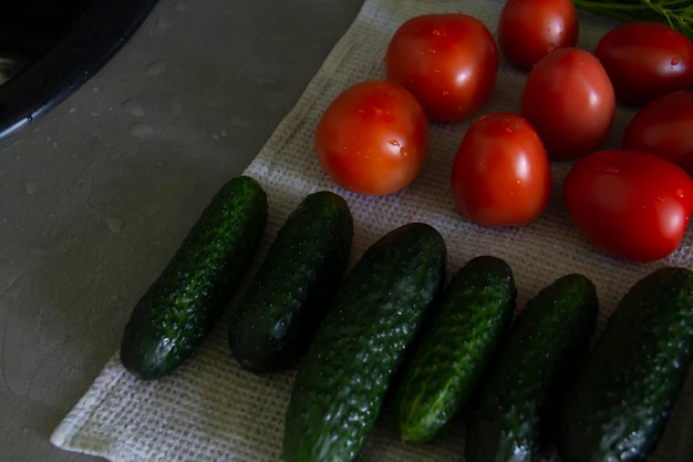 Verduras frescas pepinos tomates y verduras con eneldo y perejil se encuentran en la superficie gris de la cocina sobre una toalla de lino