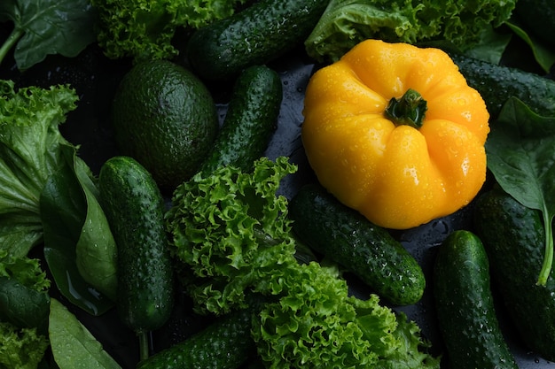 Verduras frescas, pimientos amarillos, pepino y ensalada sobre un fondo negro.