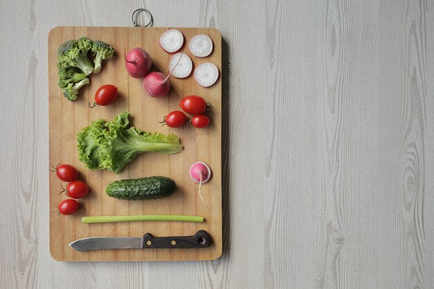 Verduras frescas en una tabla para cortar sobre una mesa de madera clara