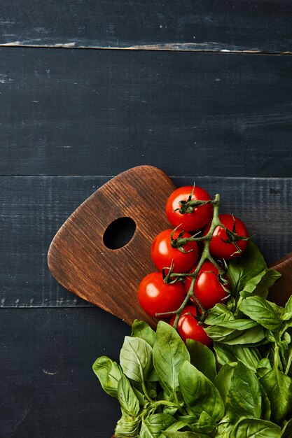 Verduras frescas tomates cherry en una rama con albahaca sobre una tabla de madera sobre un fondo de madera con un lugar debajo del texto, plano laical