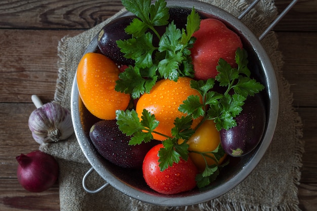 Verduras frescas con tomates perejil, berenjenas en un colador sobre una mesa de madera