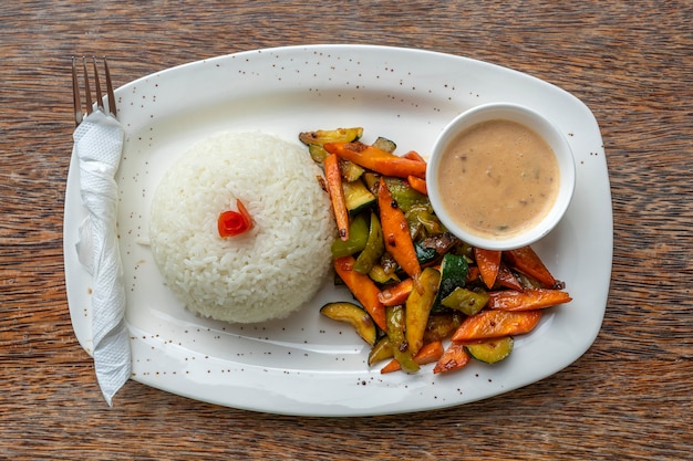 Foto verduras fritas, arroz blanco y salsa en un plato blanco