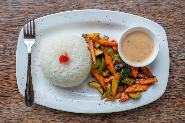 Verduras fritas arroz blanco y salsa en un plato blanco.