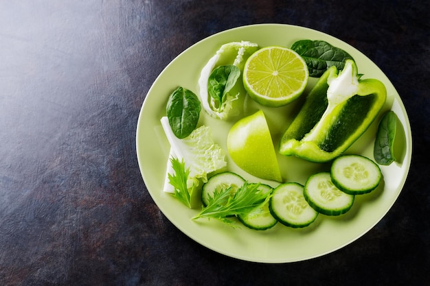 Verduras y frutas orgánicas sobre un fondo oscuro. Comida de dieta verde en un plato. Comida sana. Vista superior. Copia espacio